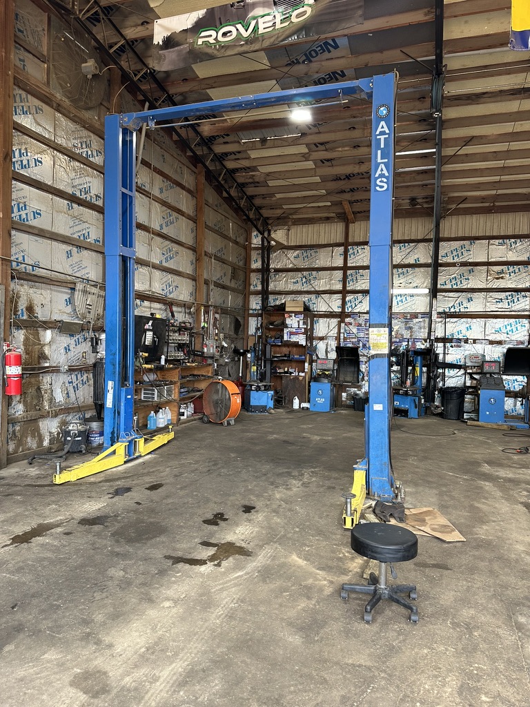 Blue and yellow Atlas two-post vehicle lift in a Hazlehurst Tire Company service bay