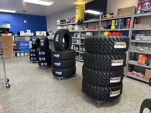 New passenger tires stacked on dollies on the retail floor at Hazlehurst Tire Company, with shelves of oils and parts behind them